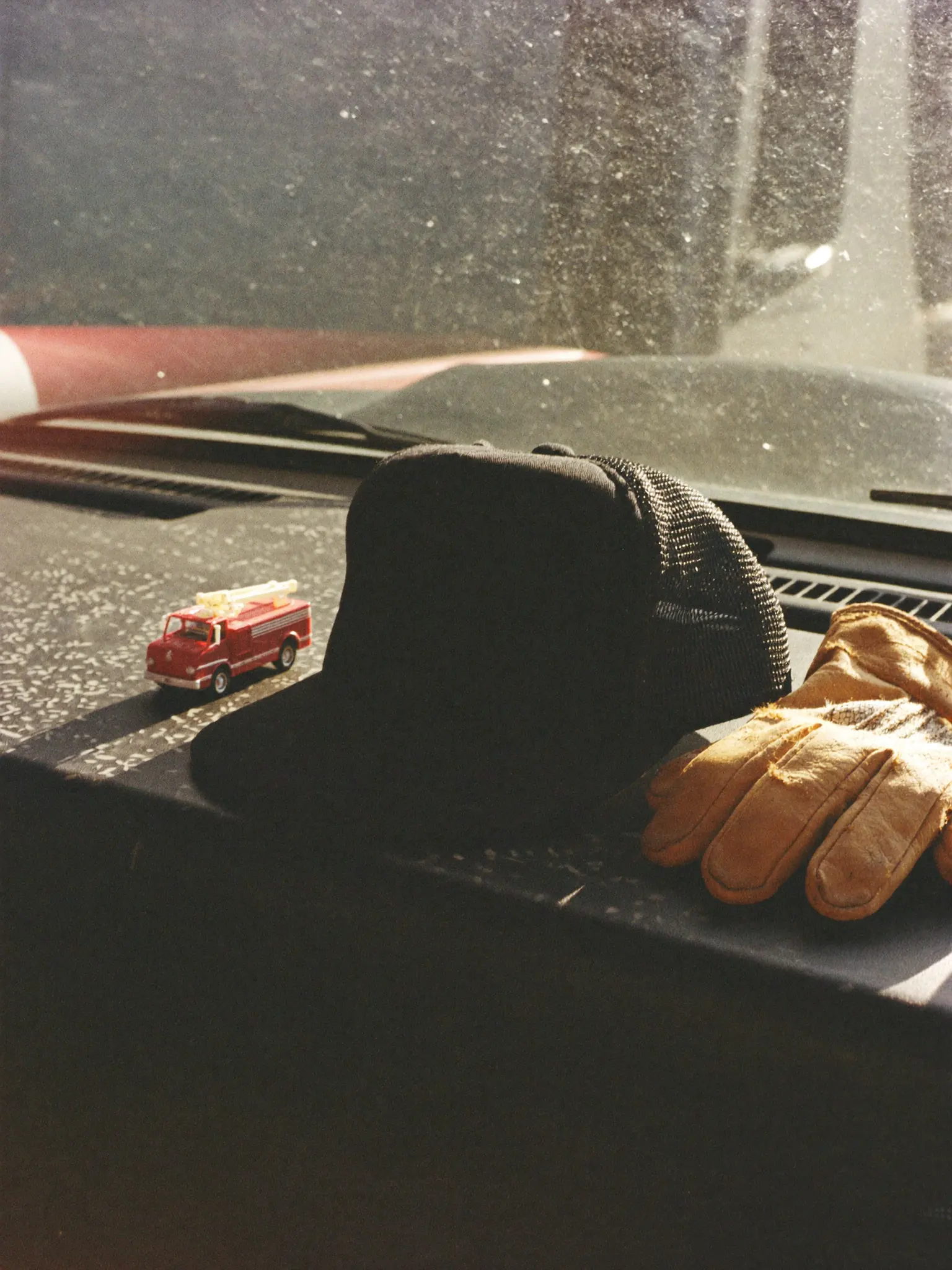 A black trucker hat, work gloves and a toy fire truck on a truck dashboard.